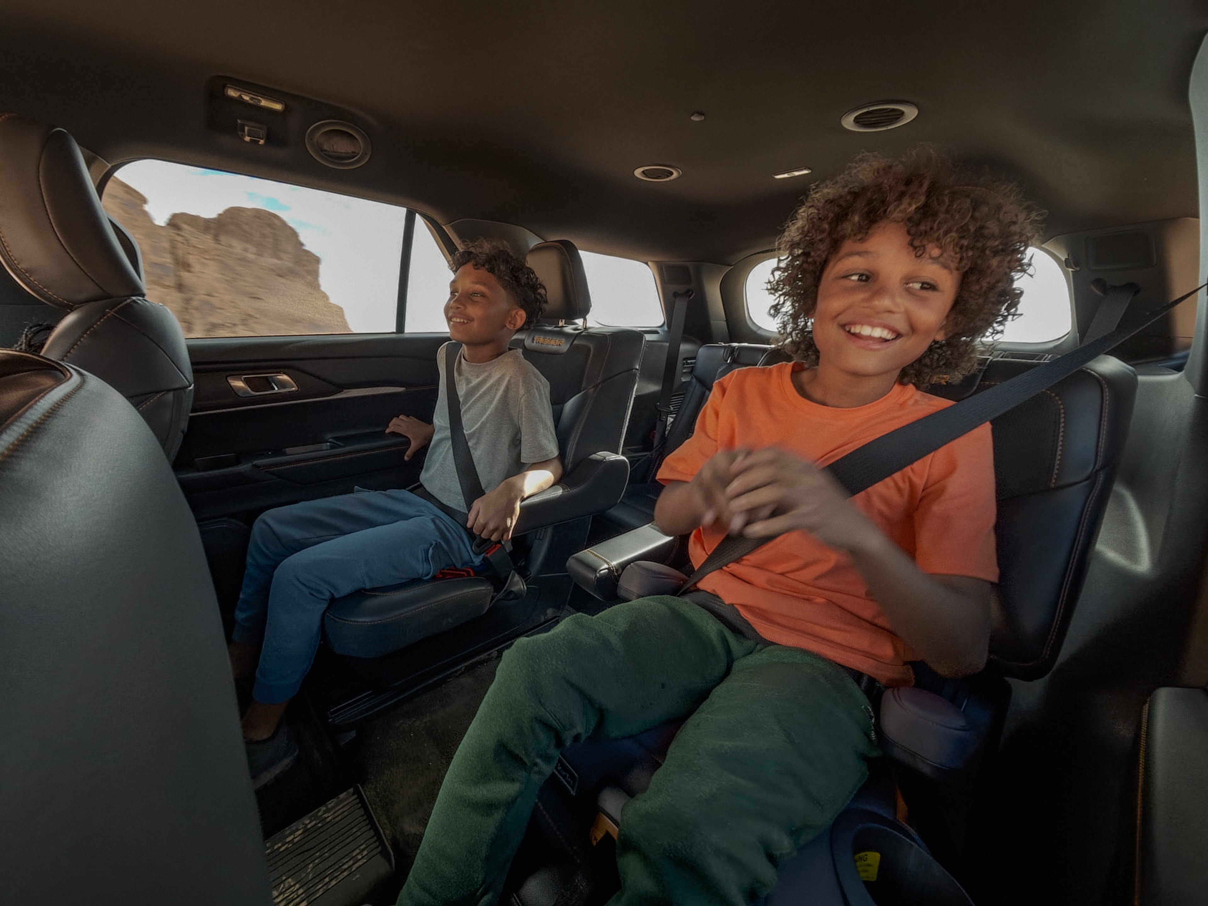 Two smiling kids sat in the back of a Ford Explorer on an off-road adventure.